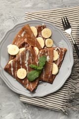Delicious chocolate crepes with banana, condensed milk and mint served on grey table, top view