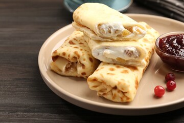 Delicious rolled crepes with cottage cheese, raisins, jam and cranberries on wooden table, closeup