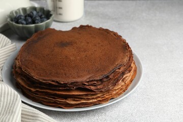 Delicious chocolate crepes with blueberries on light grey table, closeup