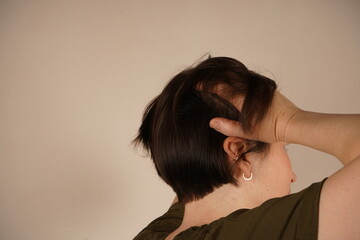 A woman with a sore head grabs her head and turns her back to the gray wall.