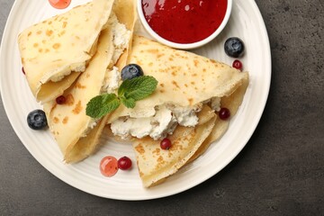 Delicious crepes with cottage cheese, jam, redcurrants and blueberries on grey table, top view