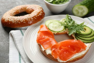 Delicious bagel with salmon, cream cheese, cucumber and avocado on grey table, closeup