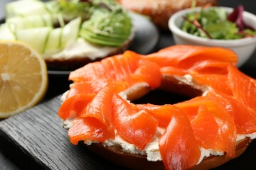 Delicious bagels with salmon and vegetables on black table, selective focus
