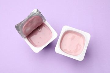 Delicious yogurts in plastic cups on violet background, flat lay