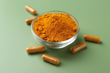 Many turmeric capsules and powder on light green background, closeup