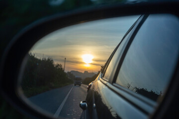 Sunset reflection in car side mirror during evening drive along a quiet road