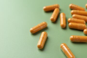 Many turmeric capsules on light green background, closeup. Space for text