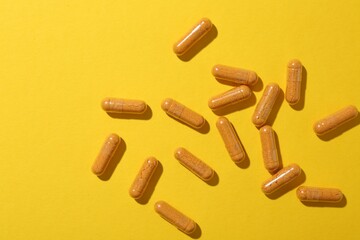 Many turmeric capsules on yellow background, flat lay