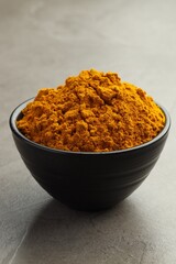 Turmeric powder in bowl on grey table, closeup