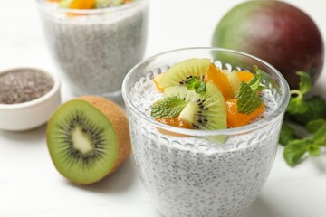 Delicious chia pudding with kiwi, peach and mint in glasses on white table, closeup