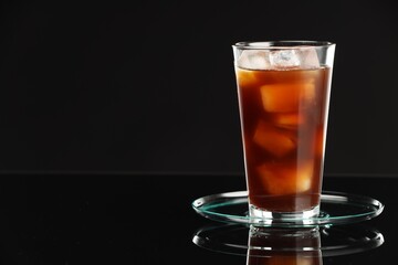 Refreshing iced coffee in glass on black mirror surface, closeup. Space for text