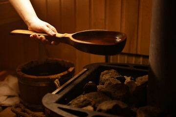 Woman pouring water on stones in sauna, closeup