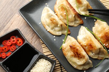 Delicious fried gyoza dumplings with sesame seeds served on wooden table, closeup