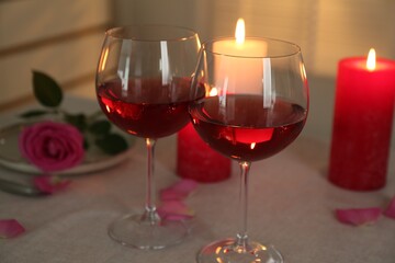Romantic place setting with red wine, burning candles and rose on table, closeup.