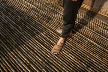 Person walking barefoot on a rustic bamboo floor during a sunny day