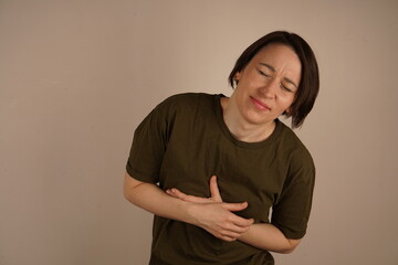 A beautiful mature woman is grimacing in pain, clutching her stomach, on a clean gray background.
