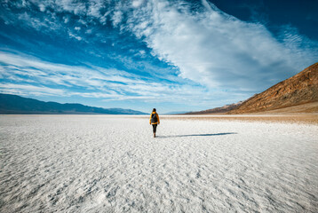 Back view of female traveler exploring death valley Badwater sighting place national park carrying backpack, young tourist woman walking in beautiful natural landscape with hot temperature
