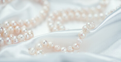 Pearl necklace over white silk background, close up. Beautiful Natural pearls beads, elegant accessories. Wedding concept, Valentine's Day Gift 