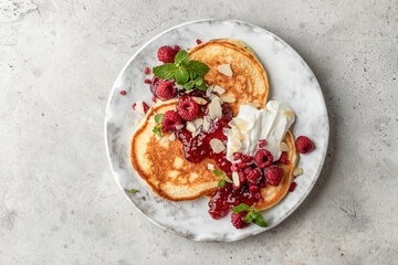 Homemade pancakes with yoghurt, berries and raspberry jam. Maslenitsa or Pancake day breakfast on gray background, top view