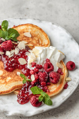 Homemade pancakes with yoghurt, berries and raspberry jam. Maslenitsa or Pancake day breakfast on gray background close up