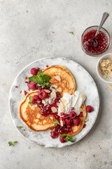 Homemade pancakes with yoghurt, berries and raspberry jam. Maslenitsa or Pancake day breakfast on gray background, top view