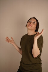A brunette with brown hair and daytime makeup in a t-shirt on a beige background spread her hands...