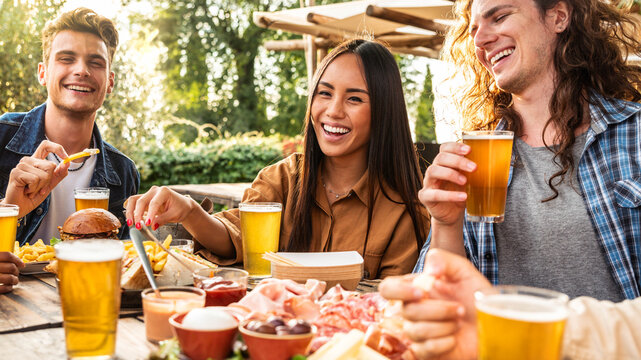 Happy multi-ethnic friends dining together at brewery pub restaurant - Young people having summer garden party eating food and drinking beer - Focus on asian women - Powered by Adobe