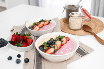 Presented by fruits putting yogurt toppings with strawberry, berry, oats, raisins and chia seed decorated by peppermint in white blow. Pink background. Set of healthy dairy product choice. Pecuniary.