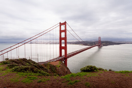 Iconic Golden Gate Bridge spans tranquil waters under moody clouds in San Francisco.