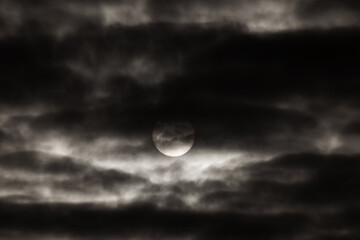 The big sun is shining through a dark stormy sky. An impressive landscape of thunderclouds as an abstract background