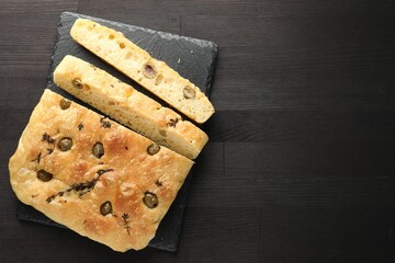 Pieces of delicious focaccia bread with olives and thyme on dark wooden table, top view. Space for text