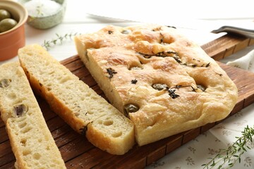 Pieces of delicious focaccia bread with olives, thyme and salt on table, closeup