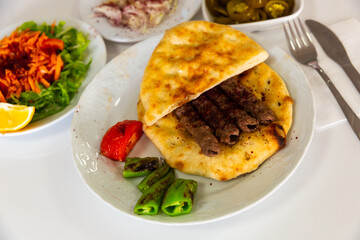 Turkish shish kofte kebab with vegetables and lavash on white plate