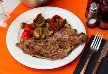 Beef steak with fried potato and vegetables dished up in a plate on the laid restaurant table