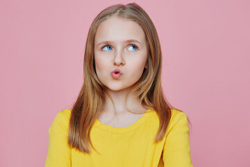 Young girl with long hair making a playful facial expression, wearing a bright yellow shirt against...