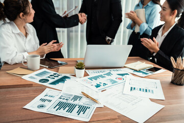 Fototapeta premium Focus financial data dashboard paper by business intelligence display graph, chart and statistic report on office table with blurred business people shake hand in corporate background. Habiliment