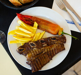 Delicious grilled veal ribs served with vegetable garnish of sweet peppers and fried potatoes