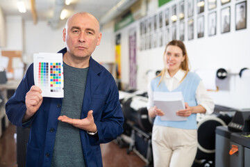 Portrait of man publishing facility worker showing colour test page and making presenting gesture.