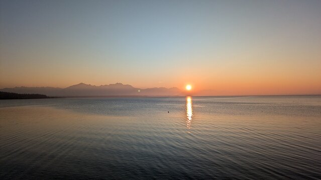 A breathtaking sunset over Lake Chiemsee, captured from Chieming, paints the sky in warm colors while the calm water reflects the glowing hues.