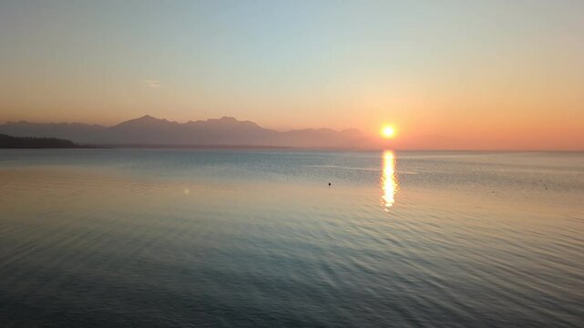 A breathtaking sunset over Lake Chiemsee, captured from Chieming, paints the sky in warm colors while the calm water reflects the glowing hues.
