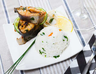 Delicious baked trout steaks with rice, grilled onions and lime served on white plate..