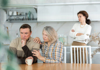 Family members quarreling in the kitchen and old woman trying to calm angry man sitting at the table
