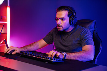 Smart gaming streamer concentrating gaming players trying to pass the level at mission completed, using headset and mic for communicate others on streaming live at neon lighting studio room. Surmise.