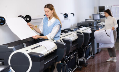 Female print worker controlling printing process on modern offset machine in print shop