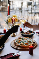 Elegant toast with white wine at a candlelit dinner, celebrating with gourmet pizza and fine dining