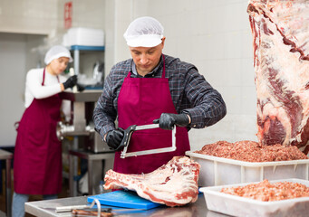 Adult male butcher sawing beef ribs with saw