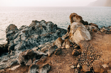 A rugged coastal landscape with weathered rocks and a calm ocean at sunset