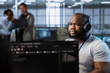 Obraz premium Engineer in server hub listening music, implementing power management solutions to reduce energy consumption. IT expert wearing headphones, hearing songs and integrating new systems in data center