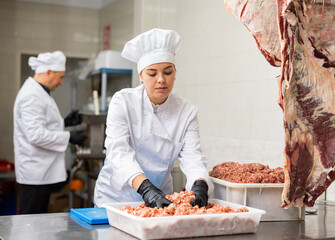 Young female butcher showing how minced meat is prepared in butchery