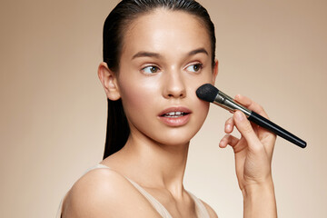 Fototapeta premium Young woman having makeup applied, showcasing a natural look with soft colors and a neutral background, highlighting beauty and self care